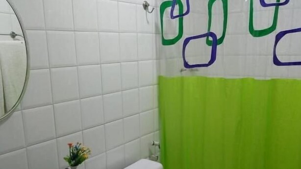 Casa de banho com paredes revestidas de azulejos brancos, lavatório preto, sanita e cortina de chuveiro verde com formas azuis e verdes.