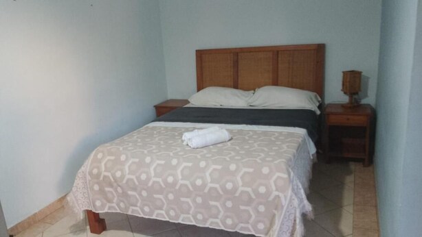 A single bed with a patterned bedspread and pillows, a wooden headboard, a bedside table with a lamp, and a tiled floor. - Pousada e Restaurante do Recreio (Rio de Janeiro)