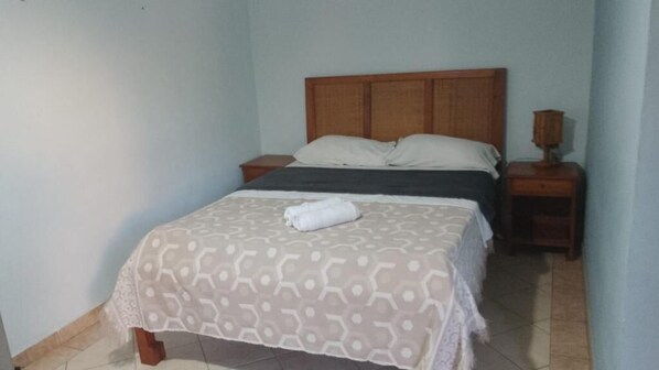 A single bed with a patterned bedspread and pillows, a wooden headboard, a bedside table with a lamp, and a tiled floor. - Pousada e Restaurante do Recreio (Rio de Janeiro)