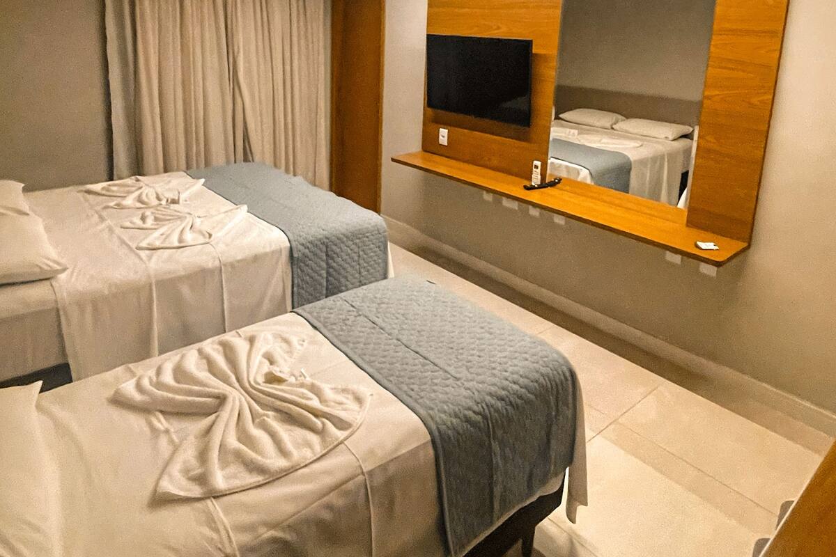 Habitación de hotel con dos camas, un televisor montado en un estante de madera y una ventana con cortinas.