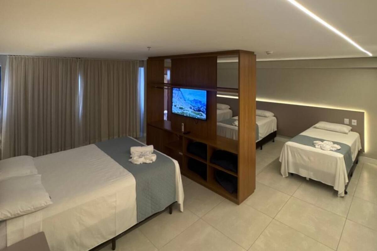 Habitación de hotel con dos camas, televisión, aparador de madera y una lámpara en el techo.