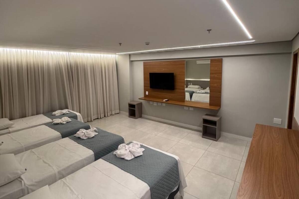 Habitación de hotel con tres camas, un televisor, un espejo y un escritorio de madera.