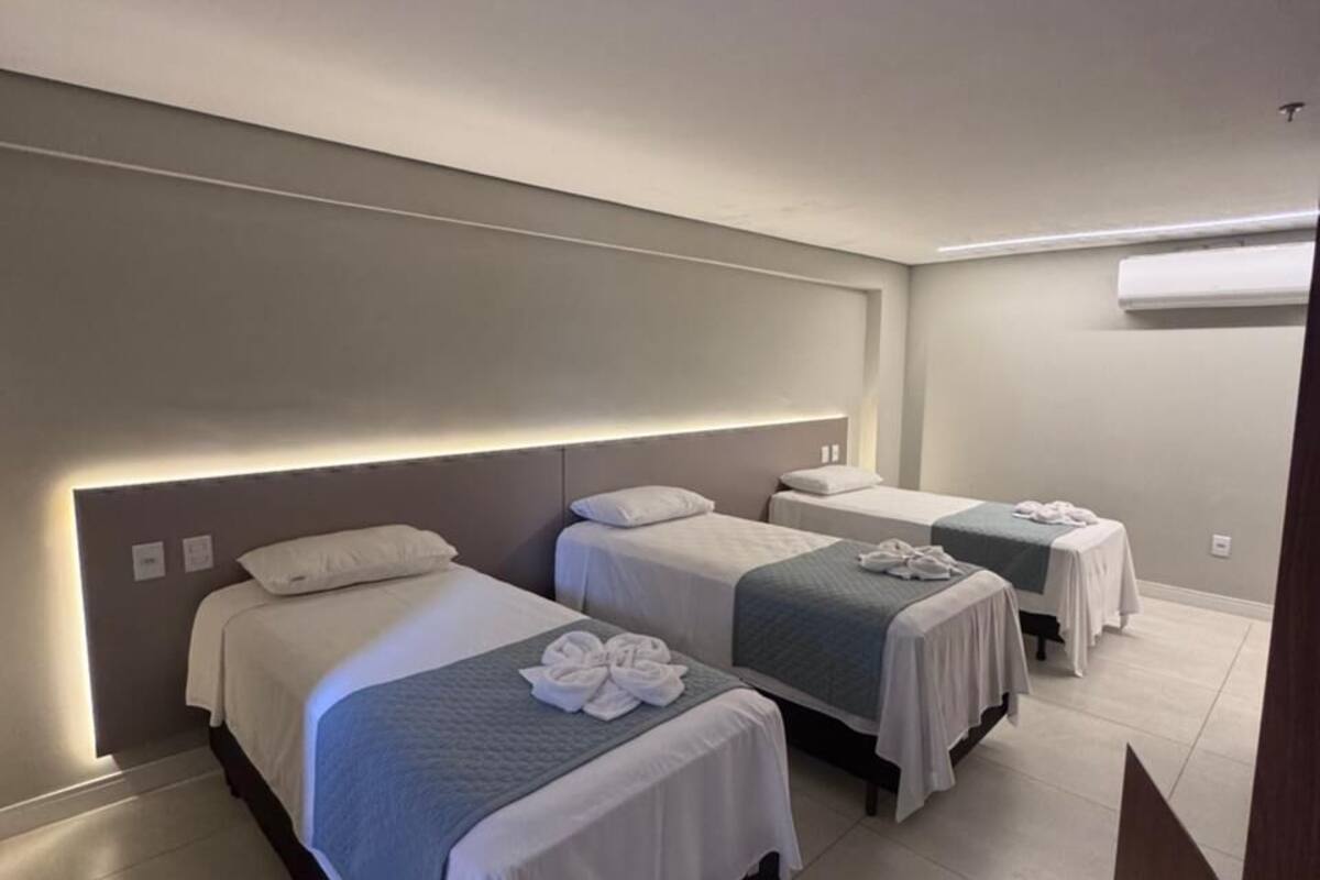 Habitación de hotel con tres camas, cada una con una colcha blanca y una toalla sobre la cama.