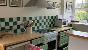 Een kleine keuken met een kookplaat, oven, magnetron en een grote afzuigkap.