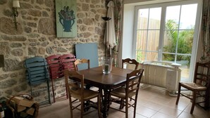 Een eetruimte met een stenen muur, een tafel met stoelen, een raam met gordijnen en een radiator.