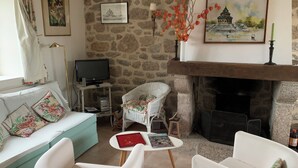 Een woonkamer met een stenen muur, een open haard, een televisie, een bank en twee stoelen.