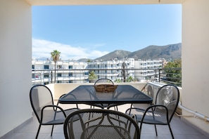 Ein Balkon mit Tisch und Stühlen, mit Blick auf eine Stadtlandschaft aus Gebäuden und Bergen.