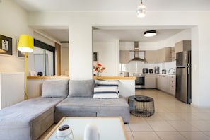 Ein modernes Wohnzimmer mit Sofa, Couchtisch, Lampe und einer Küche im Hintergrund.