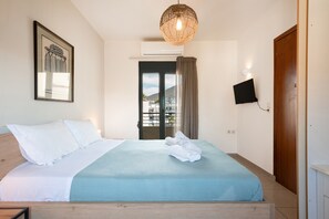 Ein Schlafzimmer mit einem Bett, einem an der Wand montierten Fernseher, einem gerahmten Bild und einem Fenster mit Vorhängen.