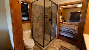 Un baño con ducha envuelta en vidrio, inodoro y cama con colcha.
