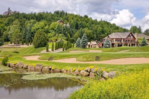 Un parcours de golf avec un étang, un chalet et une forêt environnante.