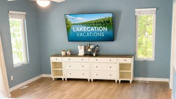 A bedroom with a bed, a dresser, a television displaying 'LAKECATION VACATIONS,' and a ceiling fan.