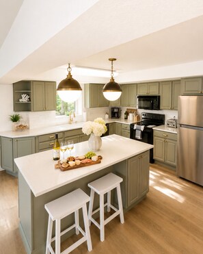 A modern kitchen with a central island, white bar stools, and green cabinetry. - Sunset Pointe Lakefront Home with Private Dock and Stunning Views (Linn Creek)
