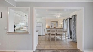 Una cocina moderna con armarios blancos, una zona de comedor con una mesa y sillas, y un espejo grande sobre la mesa.