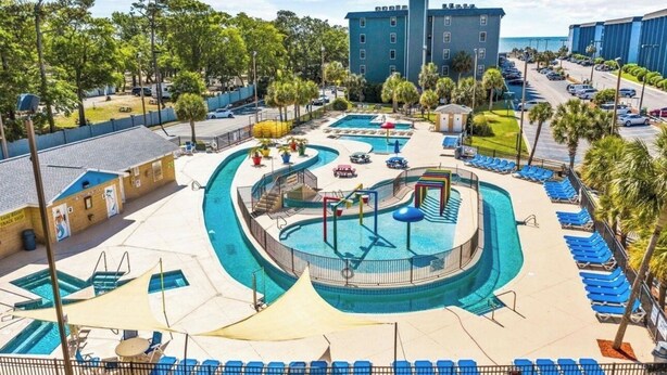Un área de piscina con varias piscinas, sillas de descanso y un edificio al fondo.