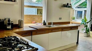 A modern kitchen with a central island, a gas stove, and a large window providing natural light. - Spacious Garden Flat- Walk to Wimbledon (London)