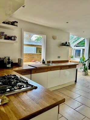 A modern kitchen with a central island, a gas stove, and a large window providing natural light. - Spacious Garden Flat- Walk to Wimbledon (London)