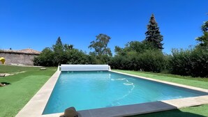 Une piscine avec un parasol blanc, un chapeau posé sur le bord et un mur de pierre en arrière-plan.