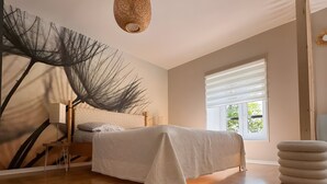 Une chambre à coucher avec un lit, une œuvre d’art murale, un luminaire suspendu et une fenêtre avec des stores.