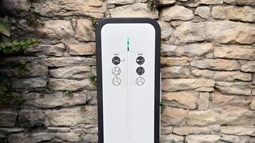 Une boîte électrique murale, dotée de boutons de démarrage et d’arrêt, est fixée sur un mur de pierres recouvert de verdure.