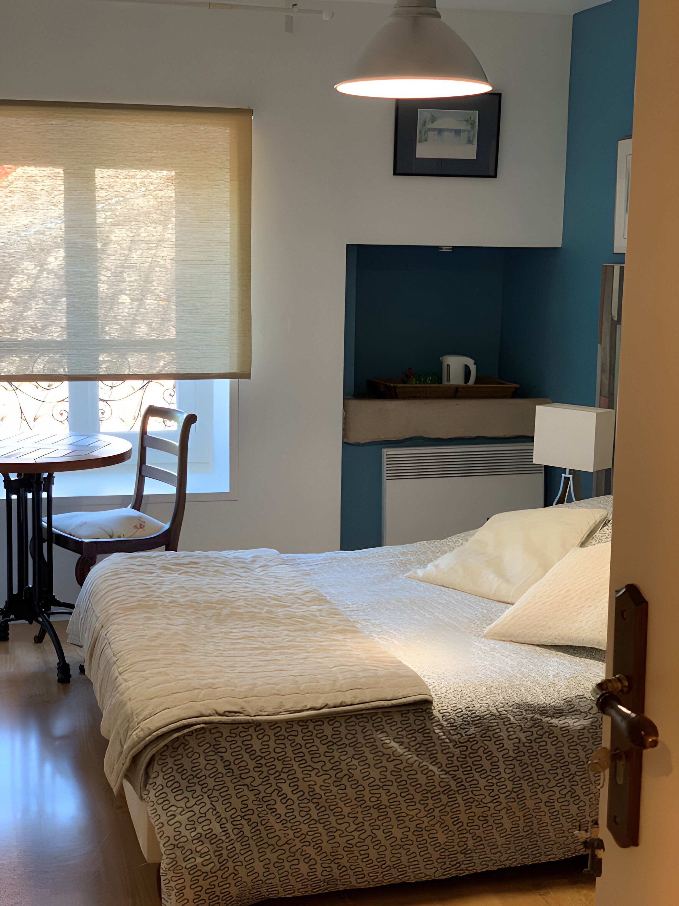 Een slaapkamer met een bed, een stoel, een tafel en een raam met jaloezieën.