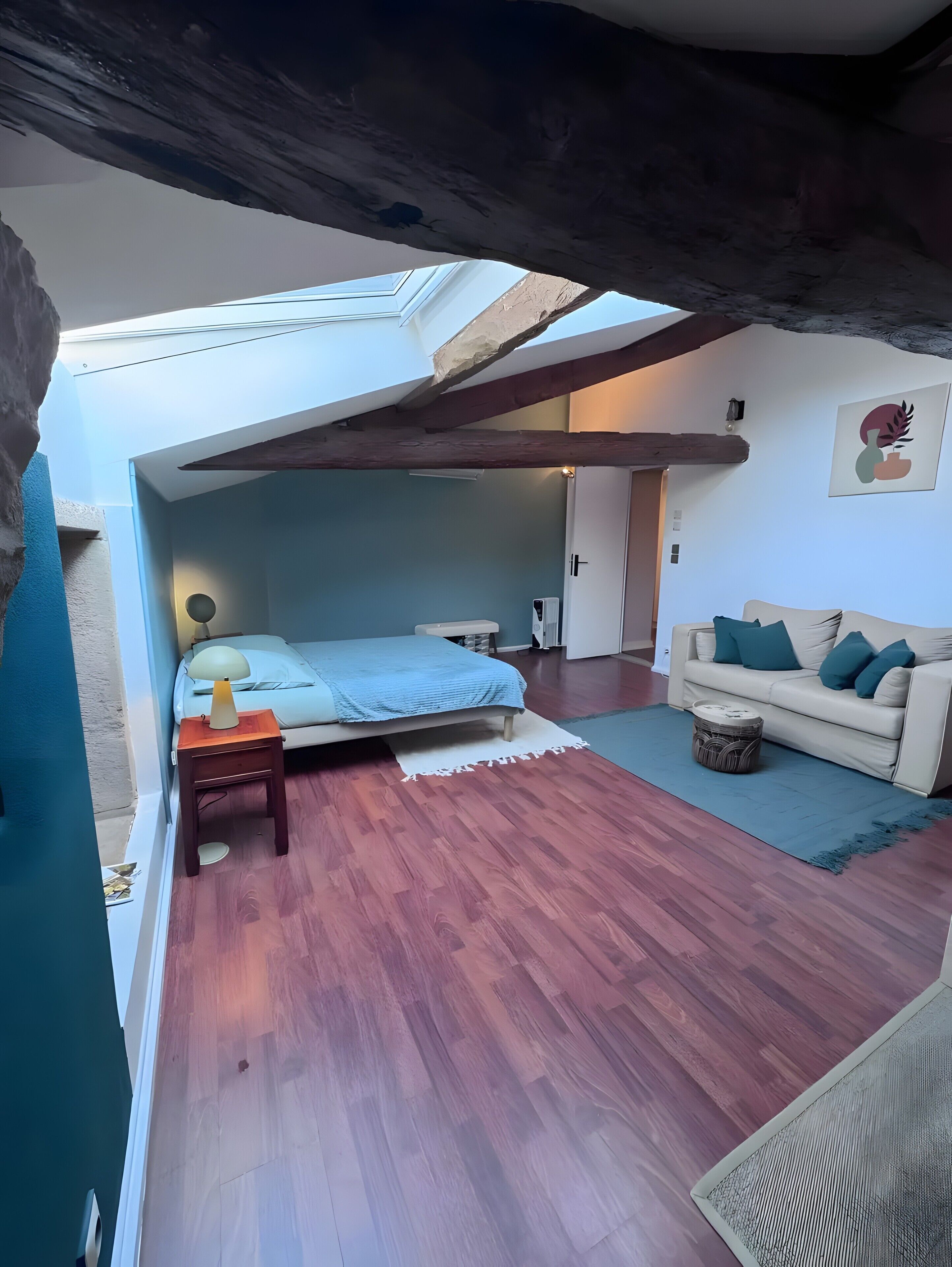 Une chambre à coucher avec un lit, une table de chevet, une lampe et une vue sur le ciel grâce à une lucarne.