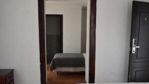 A bedroom with a bed, a dresser, and a door leading to another room.