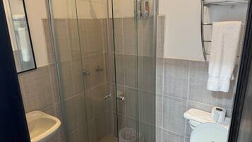 Cabina de ducha con paredes de vidrio, con inodoro y lavamanos a la derecha.