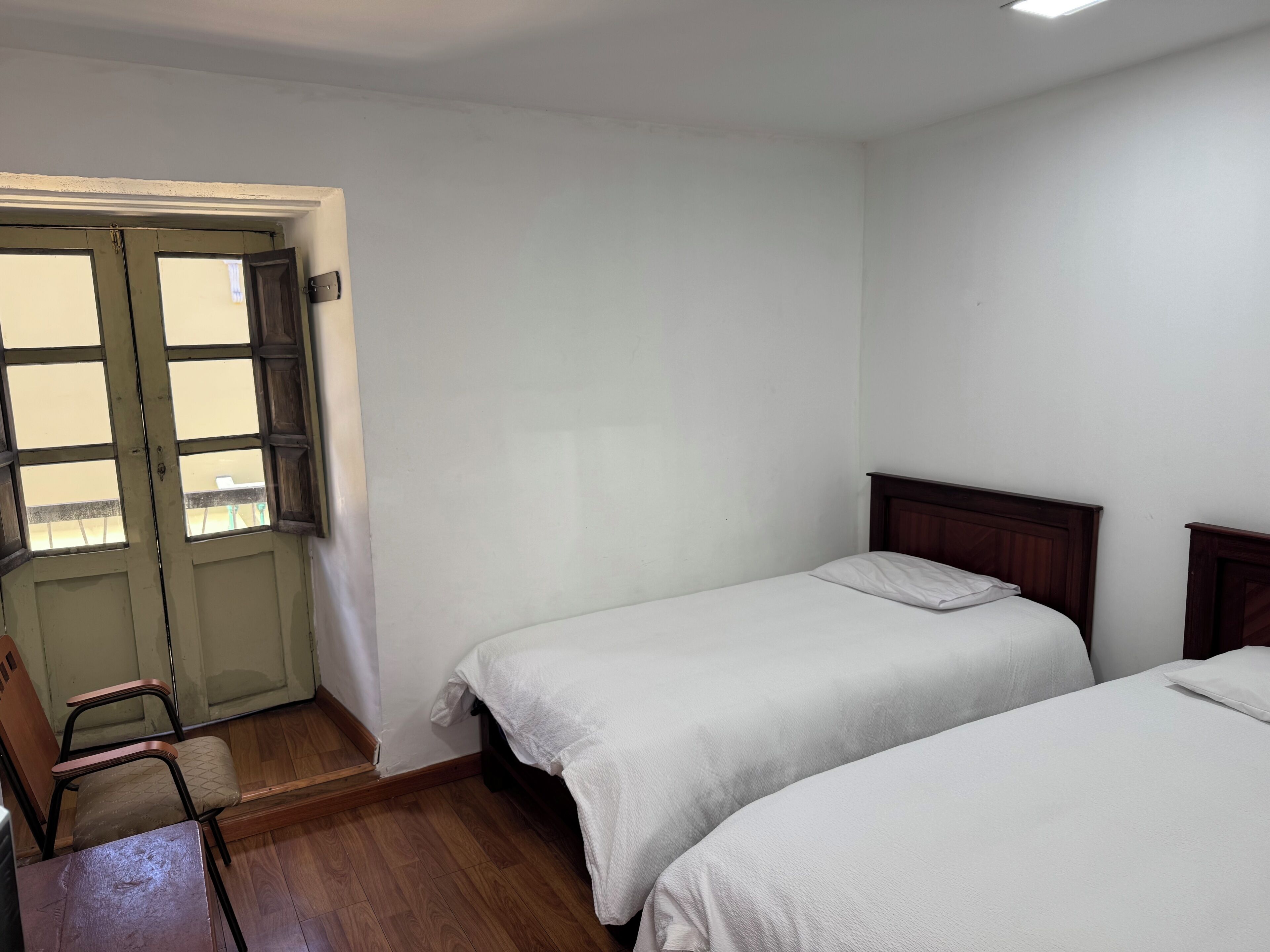 Una habitación con dos camas individuales, una silla de madera y una puerta con ventanal.