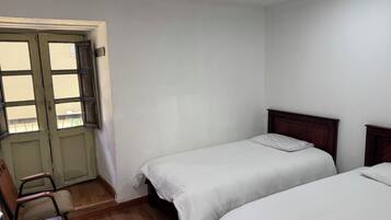 Una habitación con dos camas individuales, una silla de madera y una puerta con ventanal.