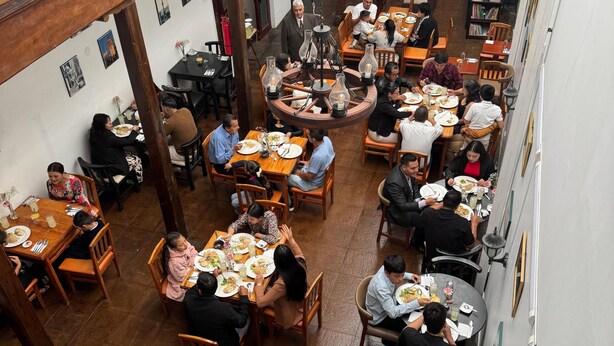 A restaurant with multiple dining tables, wooden chairs, and a central chandelier.