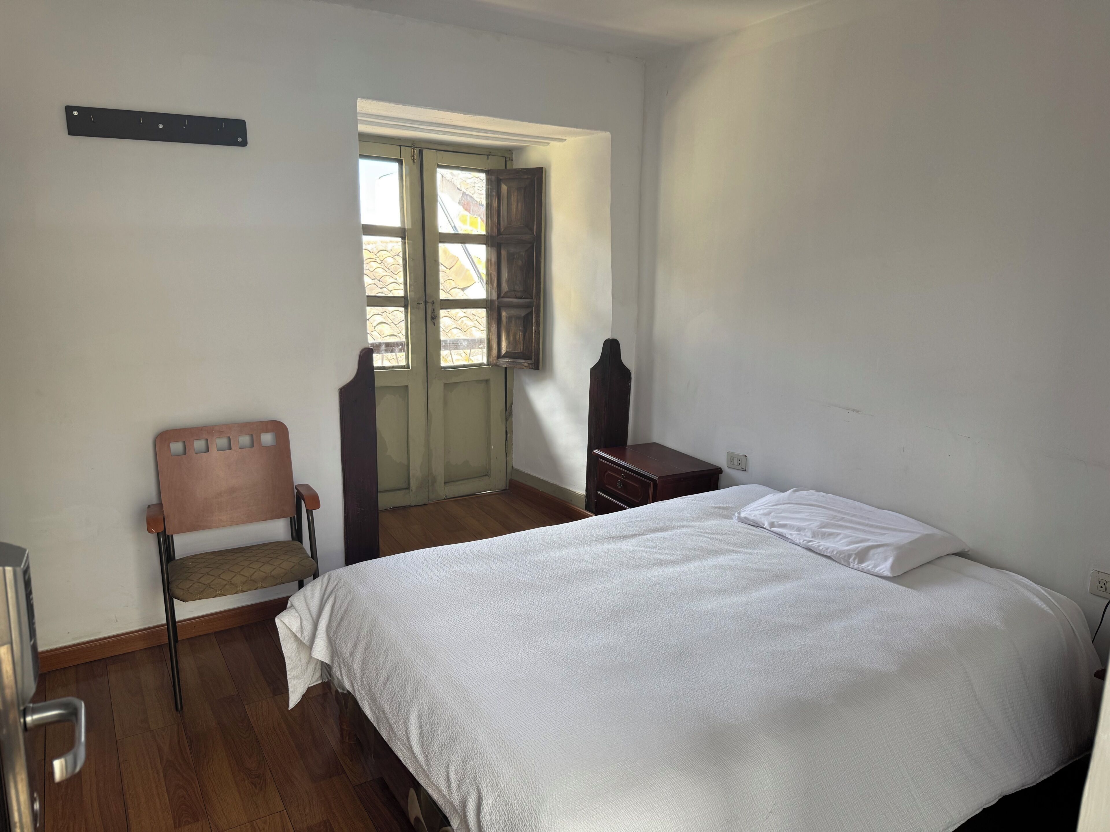 Un dormitorio con una cama, una silla, un armario de madera y una ventana.