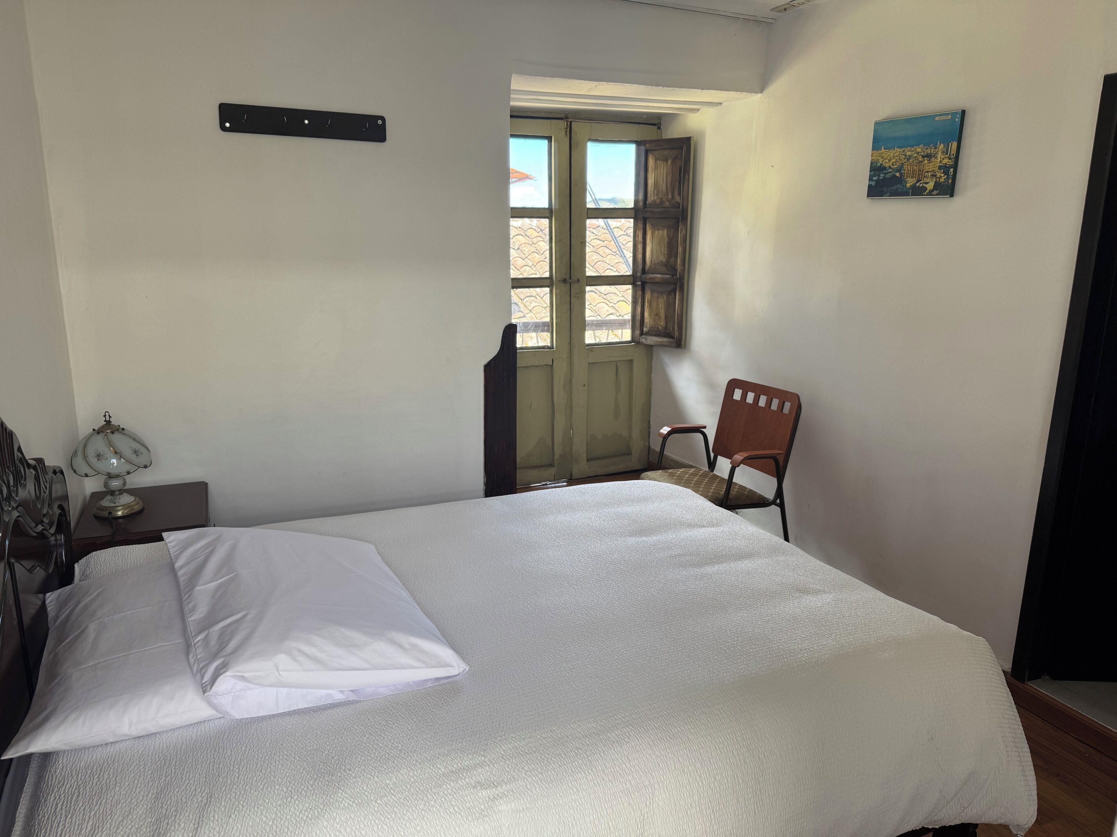 Une chambre à coucher avec un lit, une chaise, une petite table avec une lampe, une fenêtre et un tableau au mur.