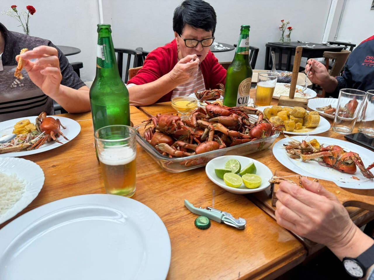 Uma mesa de jantar com vários pratos de comida, incluindo lagostas, e garrafas verdes.