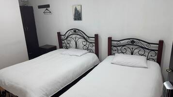 A room with two single beds, a wooden wardrobe, a small table, and a wall-mounted picture.