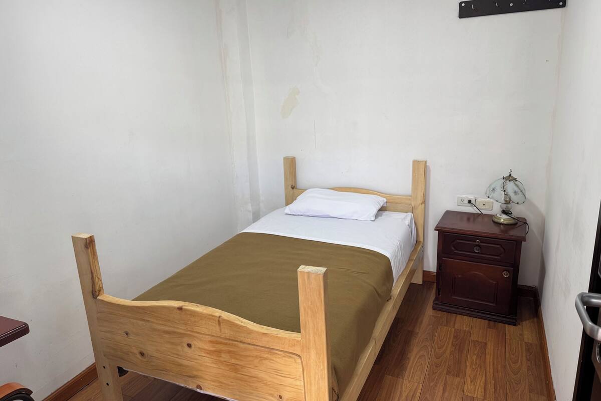 A single bed with a wooden frame, a bedside table with a lamp, and a chair.