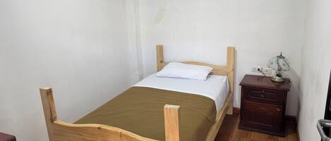 A single bed with a wooden frame, a bedside table with a lamp, and a chair.