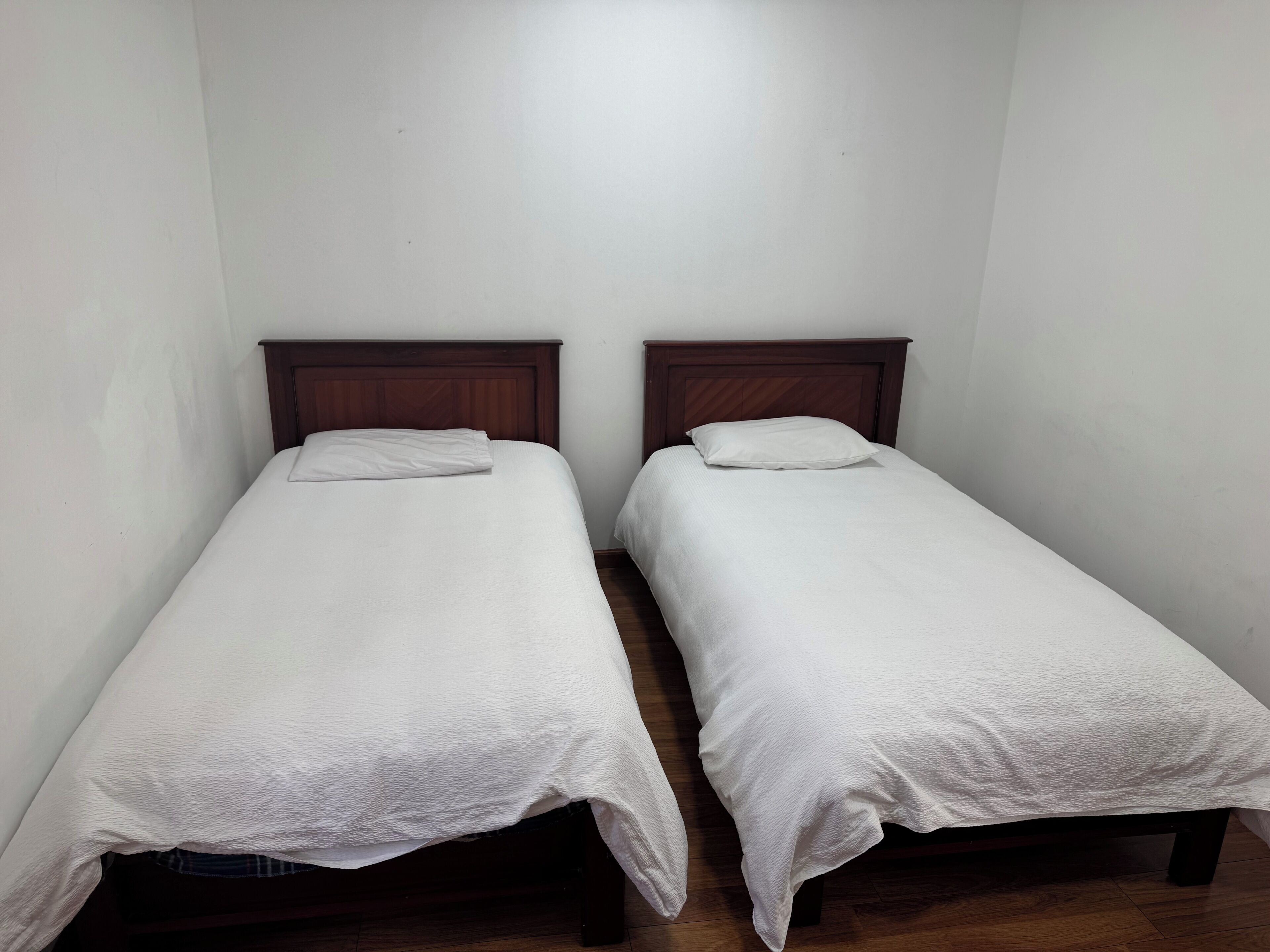 Two single beds with wooden headboards in a room with plain white walls and wooden flooring.