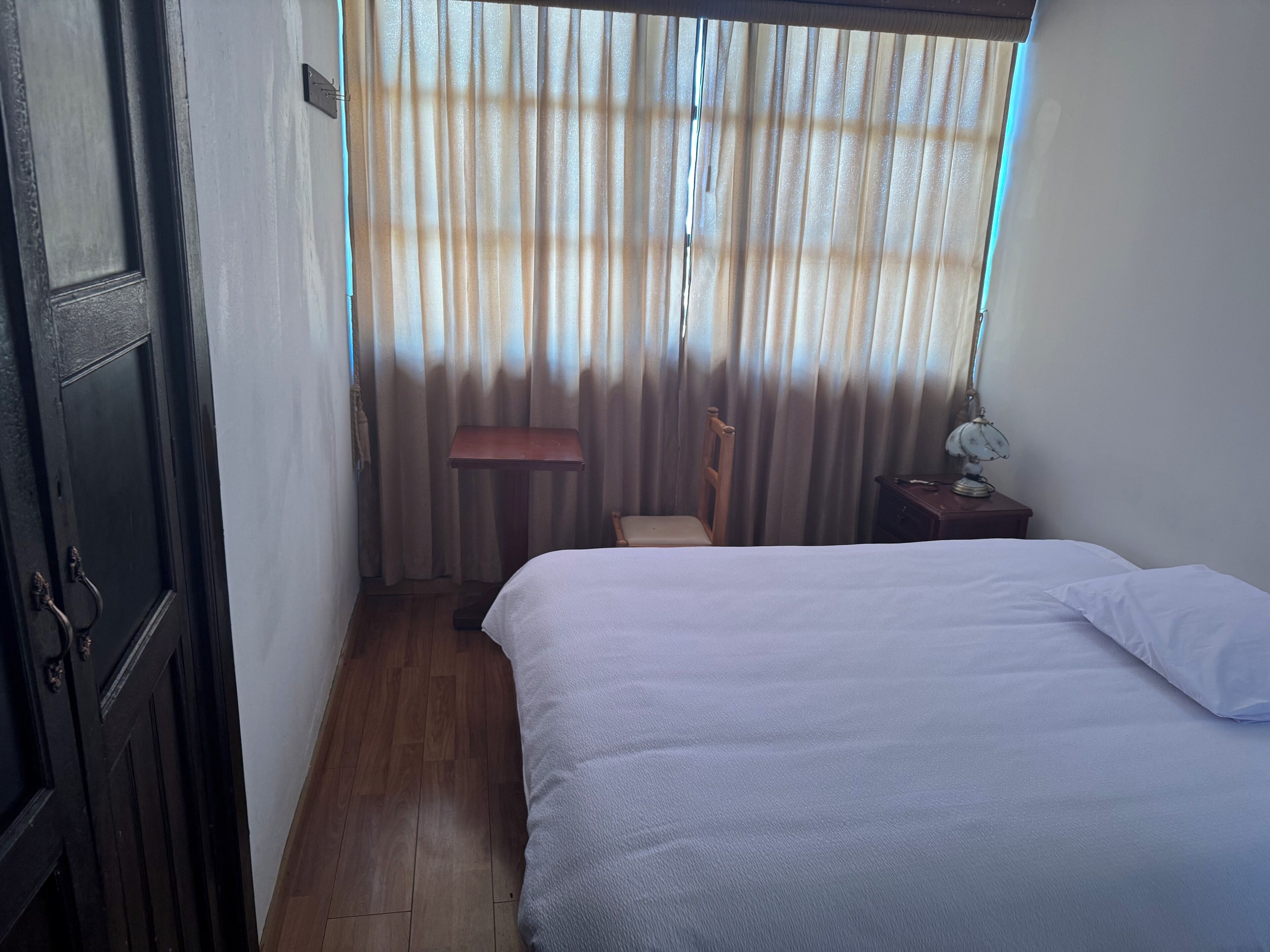 Une chambre à coucher avec un lit, une chaise, une table de chevet et une fenêtre avec des rideaux.