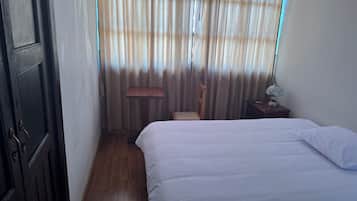 Une chambre à coucher avec un lit, une chaise, une table de chevet et une fenêtre avec des rideaux.