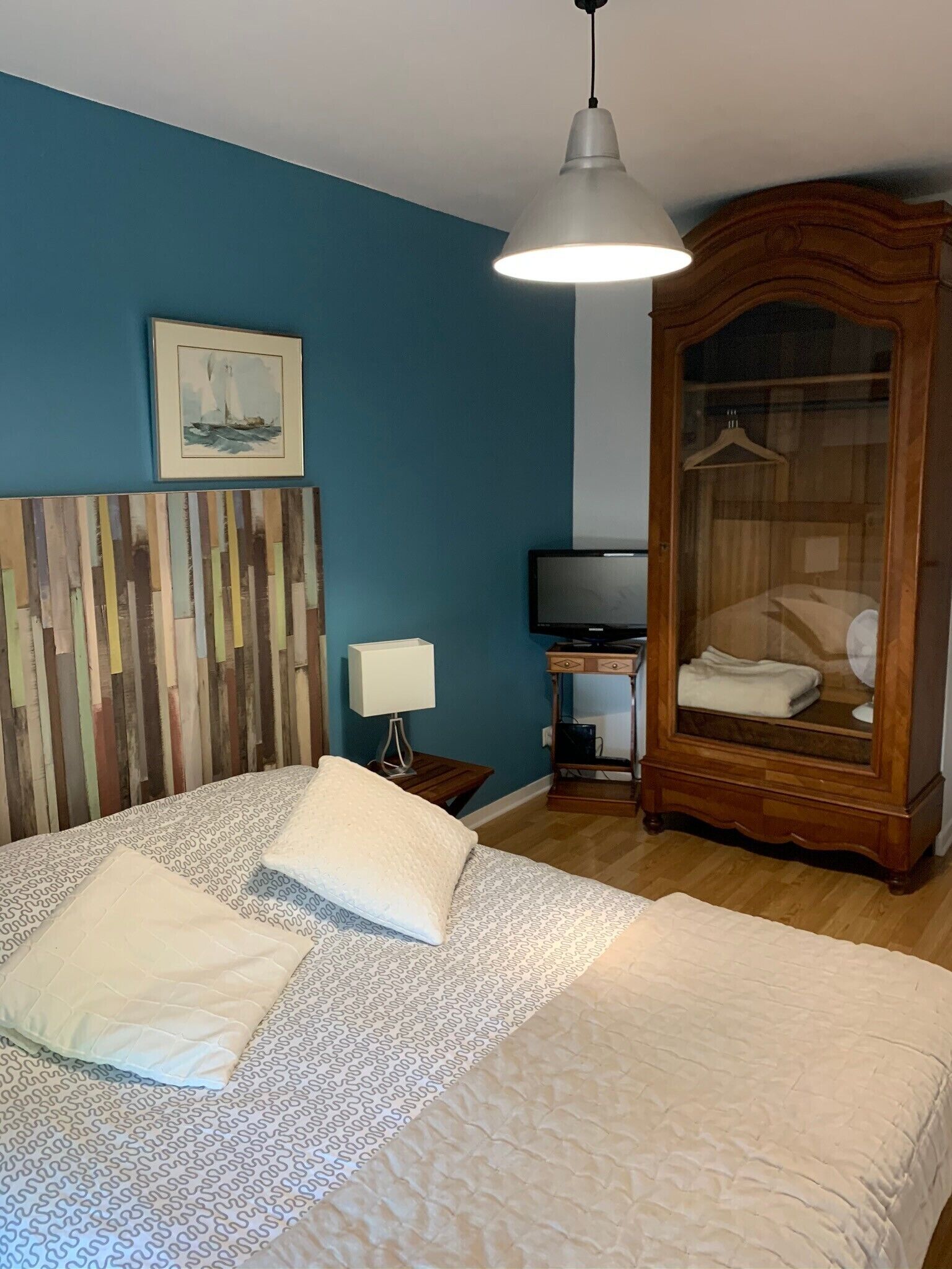 Un dormitorio con cama, mesita de noche, lámpara, televisor, armario y un cuadro en la pared.