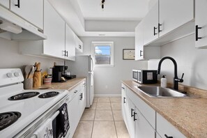 A modern kitchen with white cabinets, a stove, a microwave, and a sink. - Walkerville 2BR Suite | Near Casino & NextStar (Windsor)