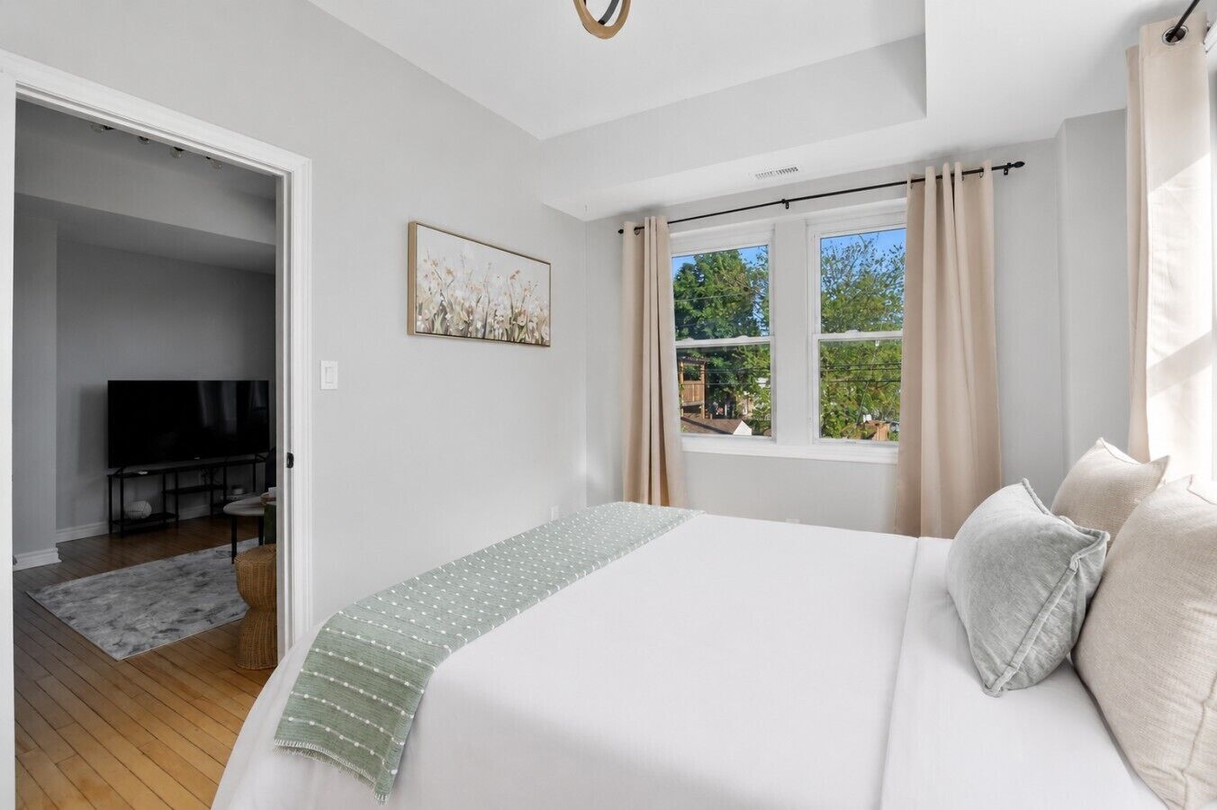 Un dormitorio con una cama, televisor, ventana con cortinas y un cuadro en la pared.