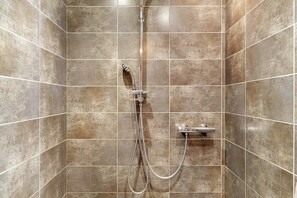 A shower with a chrome faucet and hose, tiled walls, and a corner showerhead.