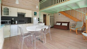 A wooden interior with a dining table, chairs, a kitchen, and a staircase.