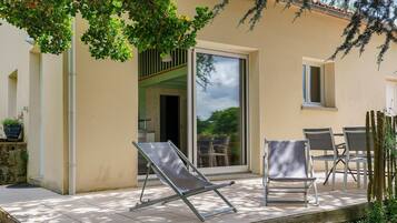 Un patio con puerta corredera de vidrio, dos sillones y una mesa con sillas.