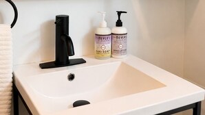 Un baño con lavamanos blanco, grifo negro, y dos botellas de jabón y crema para manos.