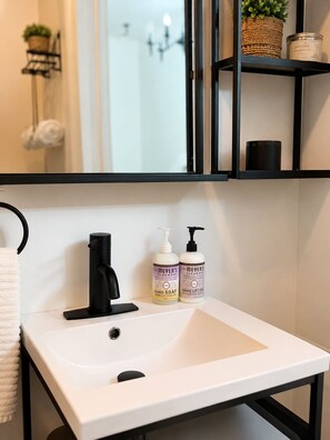 Ein Badezimmer mit einem weißen Waschbecken, einem schwarzen Wasserhahn und zwei Flaschen Handseife und Lotion.