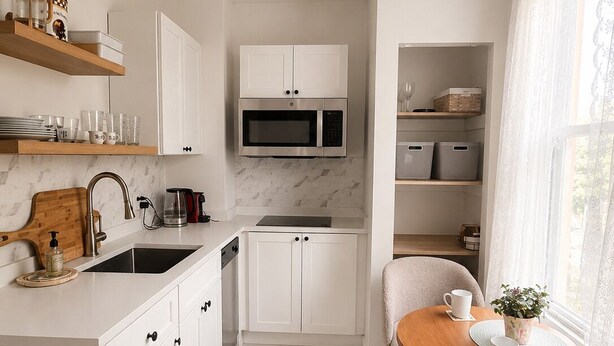 Una cocina moderna con armarios blancos, microondas integrado, ventilador de techo y comedor con mesa y sillas.