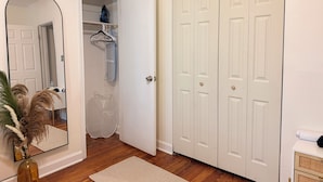 Una habitación con piso de madera, una puerta blanca, un espejo y un perchero.
